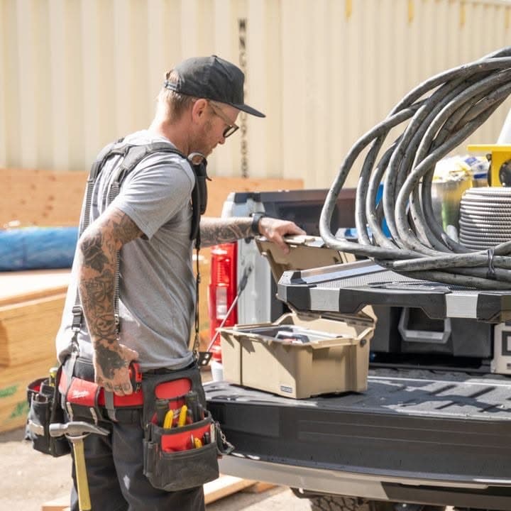 Electrician in a tool belt opening a toolbox on a drawer system in the bed of a work truck
