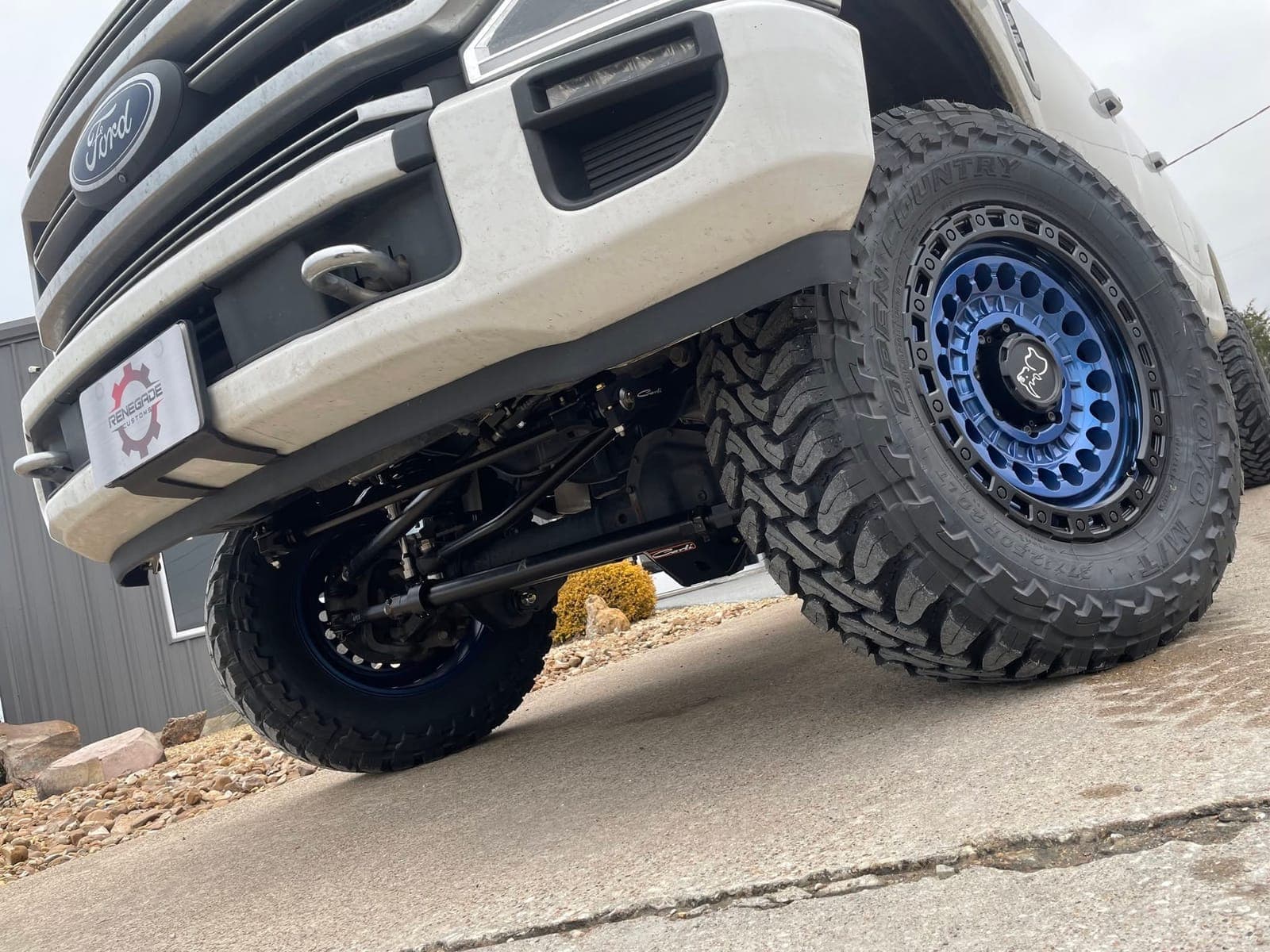 Lifted white Ford Super Duty on blue beadlock wheels and mud tires, low angle