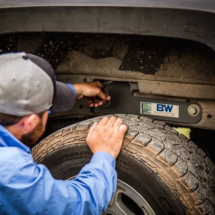 Installer mounting a B&W under-bed gooseneck hitch bracket to a truck frame