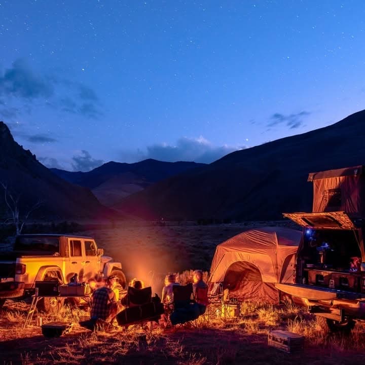 Pickup with its camper shell open beside a tent and campfire at night