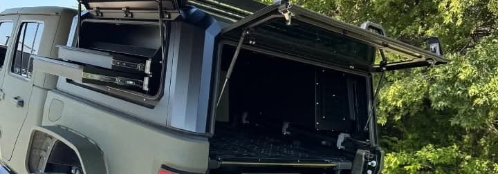 Overland camper shell with its side hatch and rear door open over bed drawers